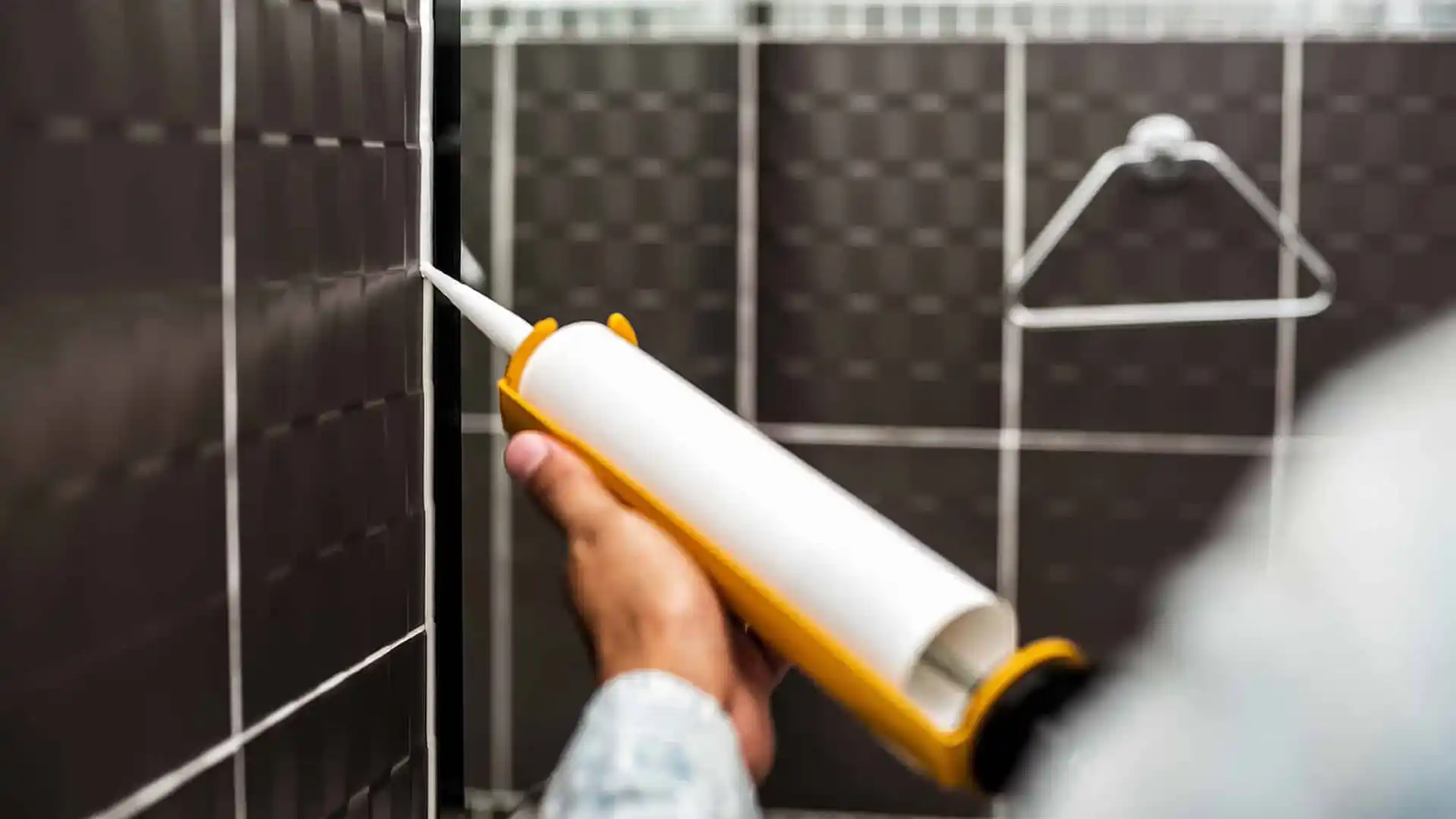 Homem aplicando um silicone acético em um box de banheiro com uma pistola aplicadora.